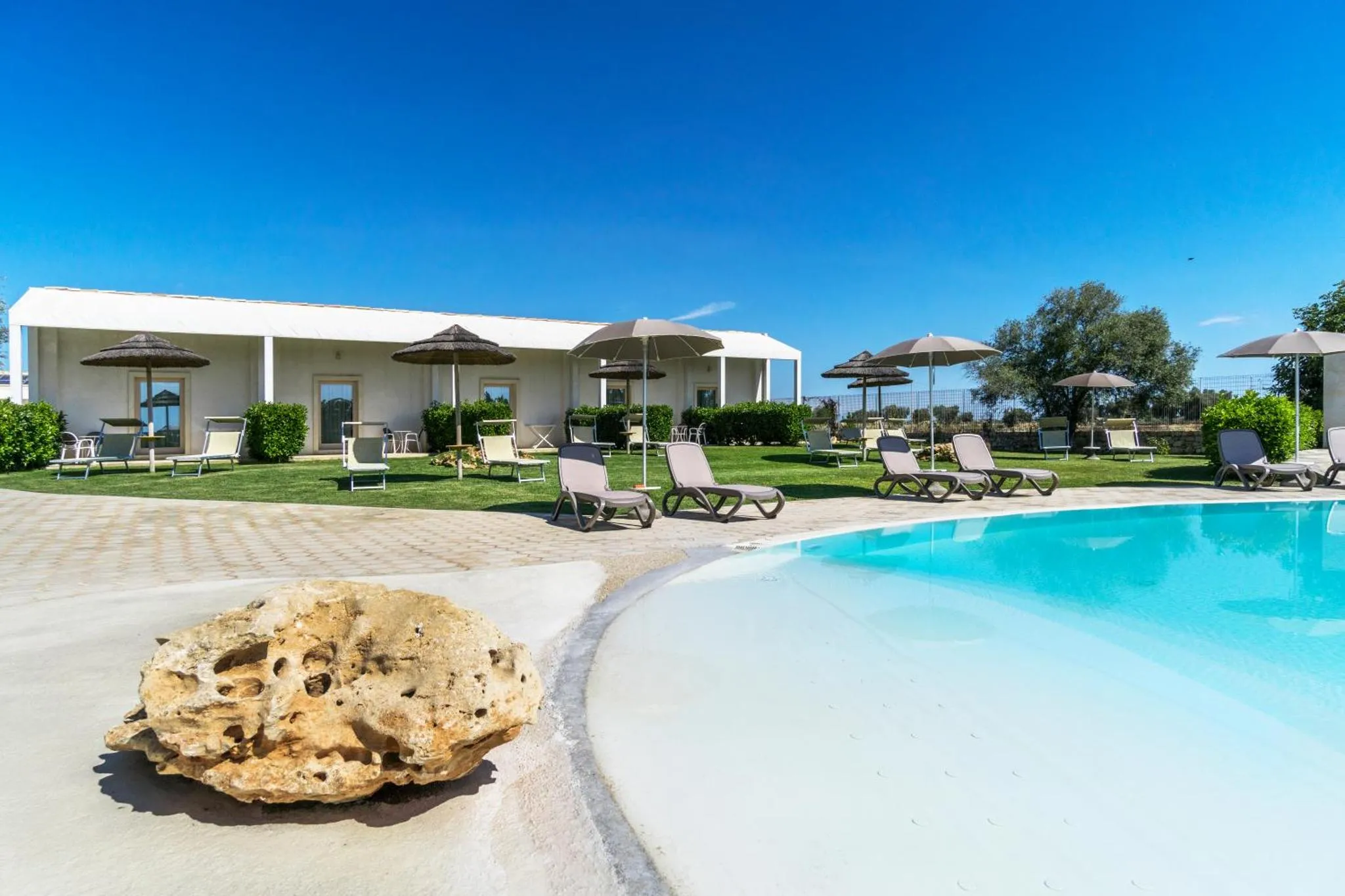 Transats et parasols bordent une piscine turquoise dans un jardin verdoyant.