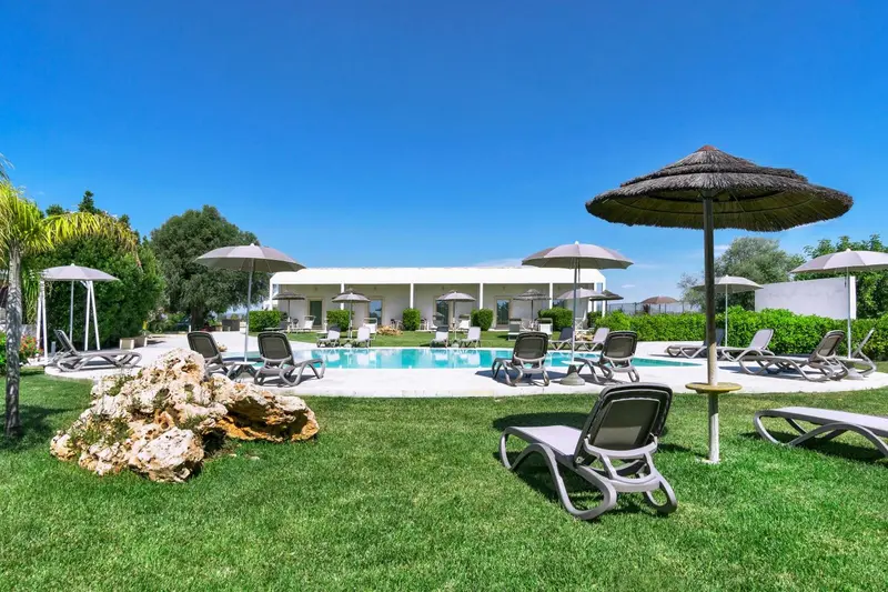 Transats et parasols bordent une piscine dans un jardin verdoyant.