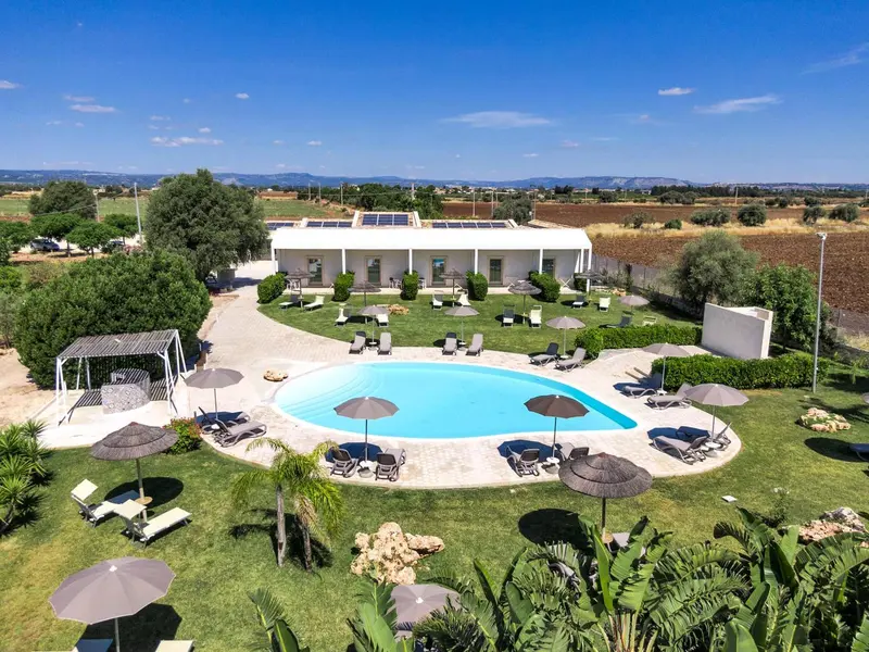 Vue aérienne d'une piscine entourée de transats et de parasols dans un jardin verdoyant.