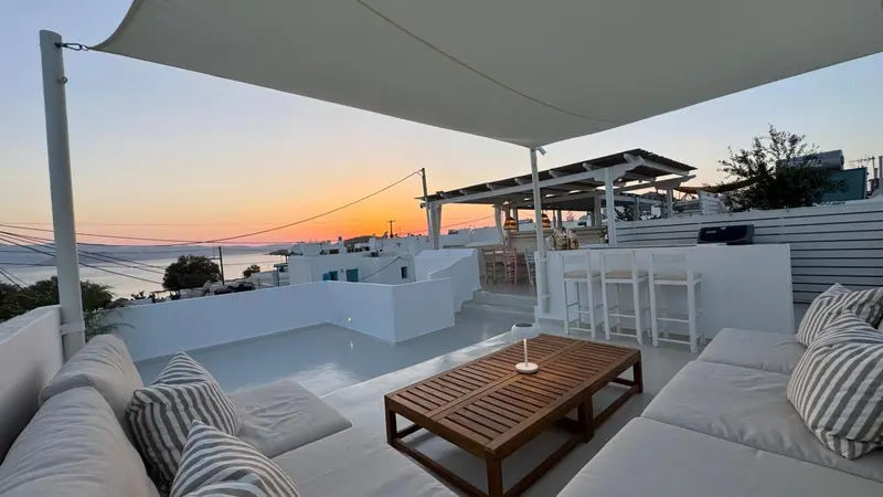 Espace de détente extérieur avec canapés et table basse face à la mer au coucher du soleil.