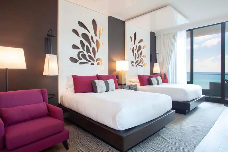 Chambre moderne avec deux lits et un fauteuil rose.