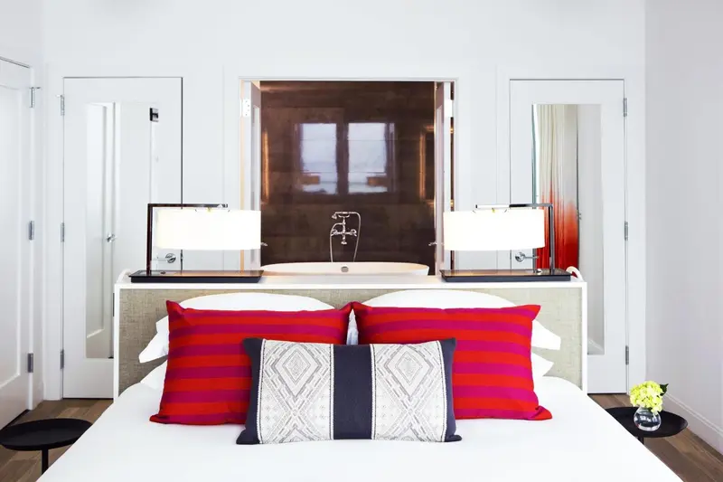 Une chambre lumineuse avec un lit recouvert d'oreillers colorés face à une baignoire.