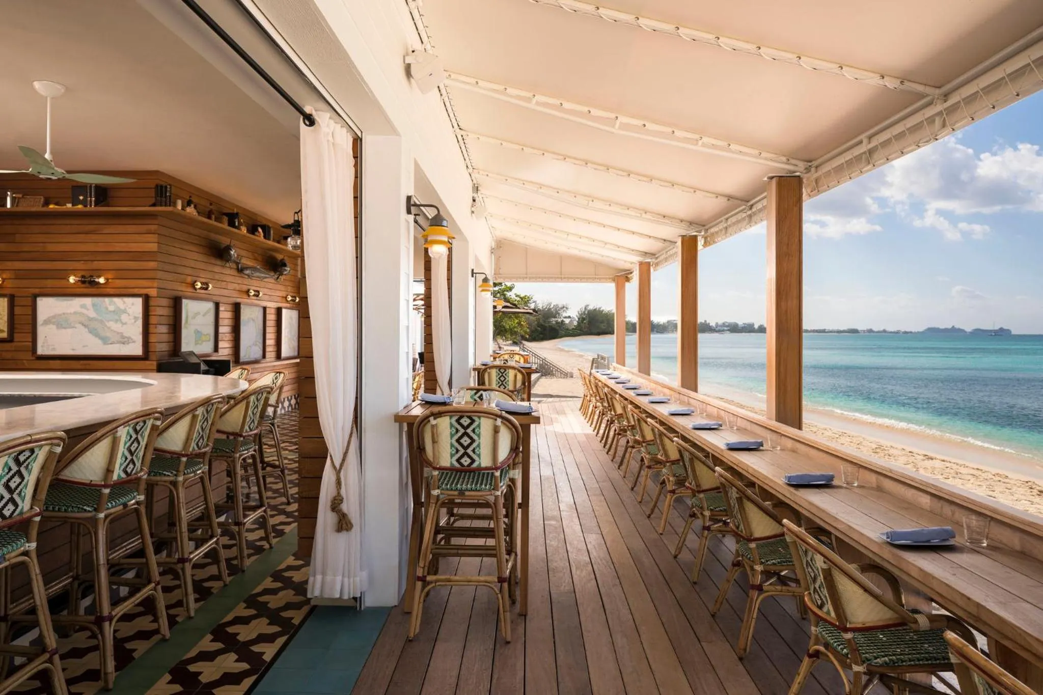 Terrasse ombragée avec bar et tables donnant sur une plage de sable fin et une mer turquoise.