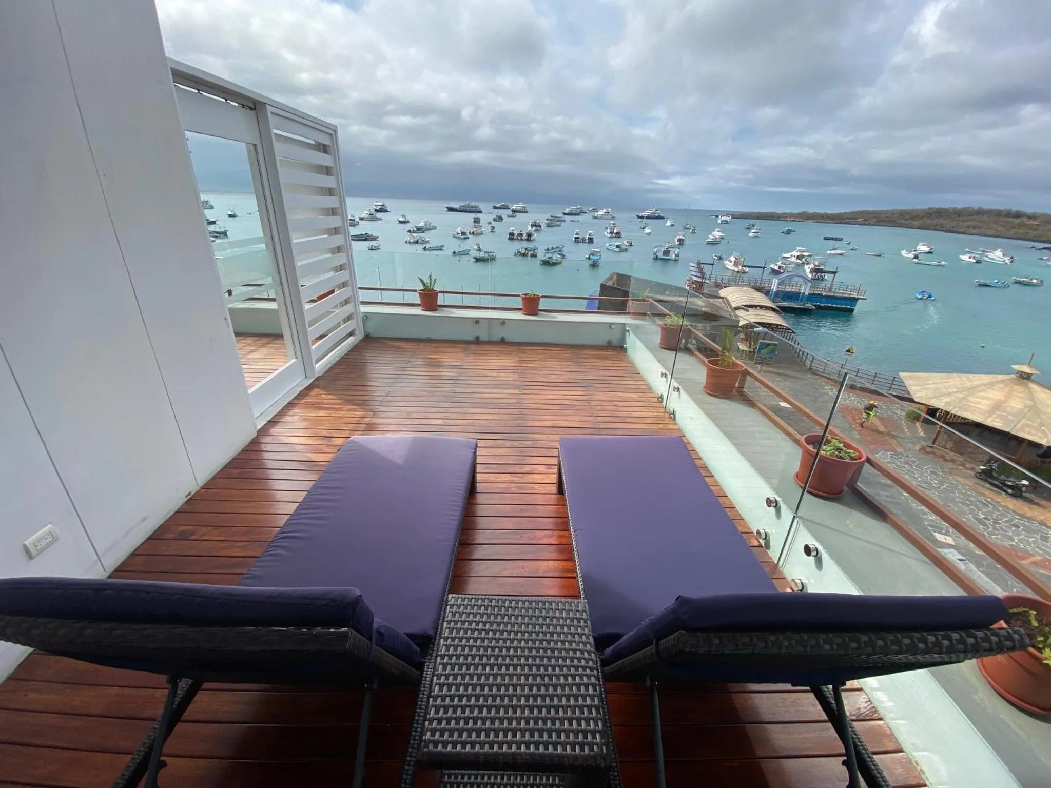 Terrasse en bois avec transats donnant sur une baie abritée et des bateaux.