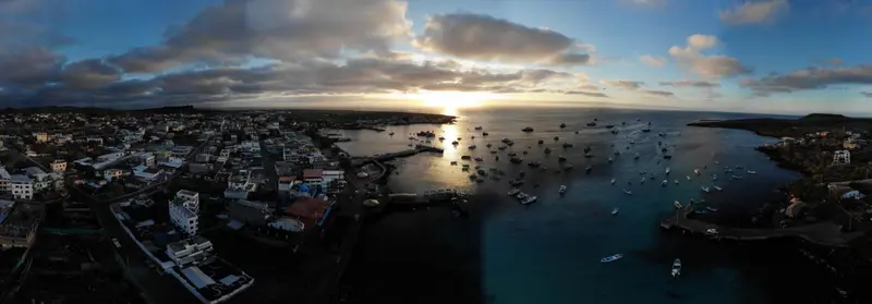 Vue aérienne d'une ville côtière avec des bateaux amarrés dans une baie au coucher du soleil.