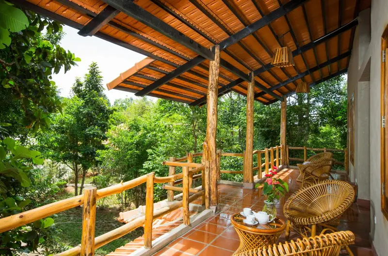 Terrasse couverte avec mobilier en rotin donnant sur une végétation luxuriante.