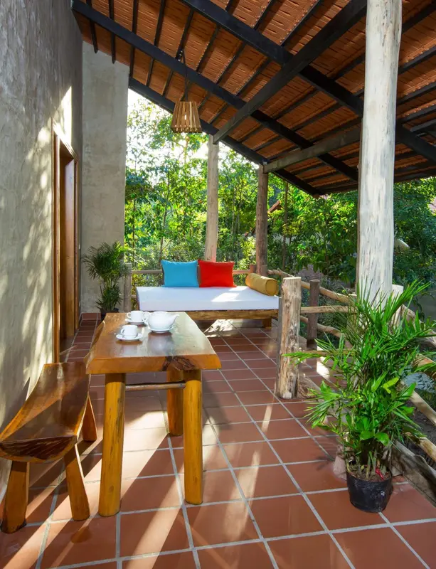 Terrasse ombragée avec table basse et coussins colorés sur un banc en bois.