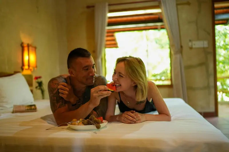 Un couple déguste des fruits sur un lit dans une chambre.