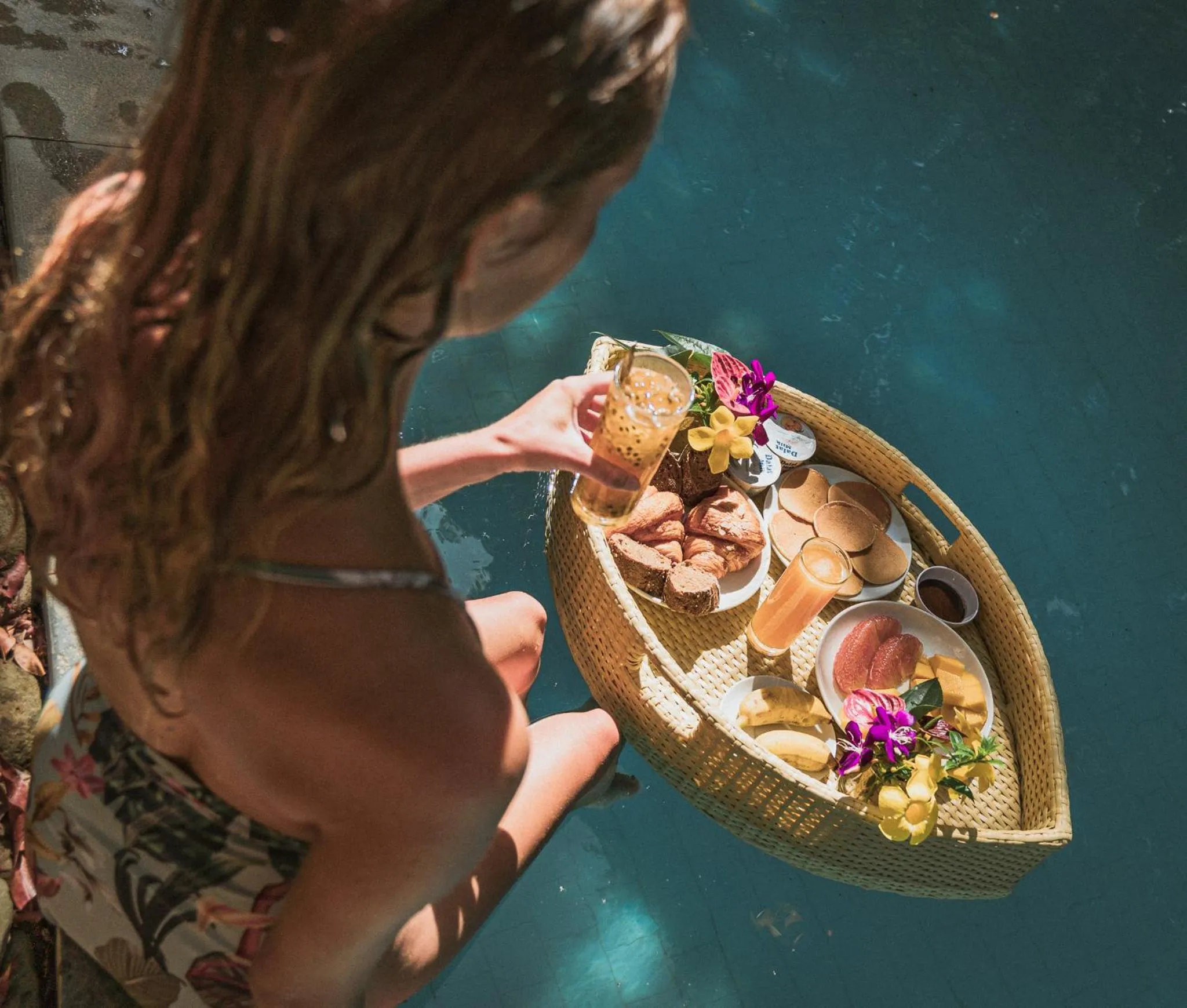 Une personne tend un plateau de nourriture et de boissons au-dessus d'une piscine.