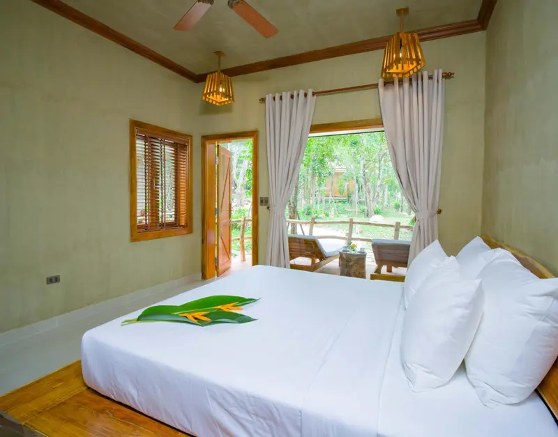 Une chambre lumineuse avec un grand lit recouvert de blanc et une vue sur une végétation luxuriante.