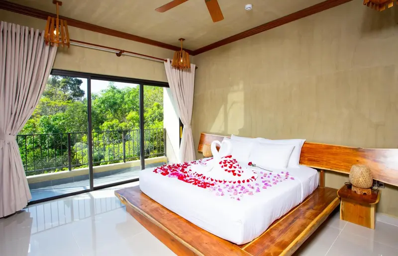 Une chambre lumineuse avec un lit décoré de pétales de fleurs et une vue sur la végétation.