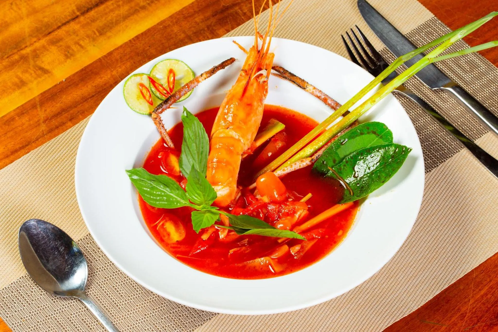 Assiette de crevettes dans une sauce rouge épicée, décorée de légumes et d'herbes fraîches.
