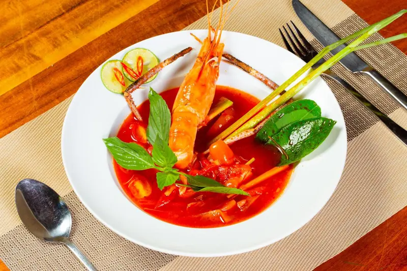 Assiette de crevettes dans une sauce rouge épicée, décorée de légumes et d'herbes fraîches.