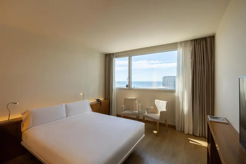 Chambre lumineuse avec un grand lit et une vue sur la mer.