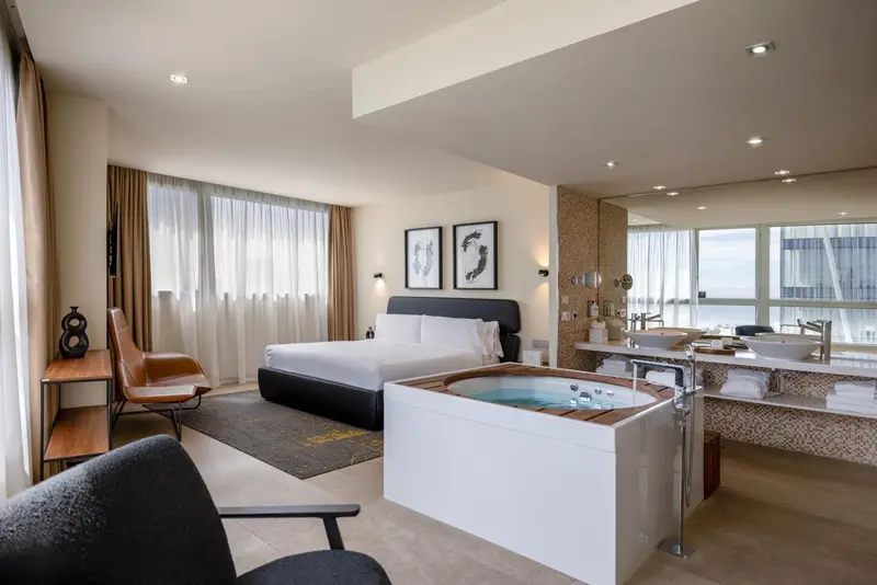 Une chambre lumineuse avec un grand lit et une baignoire jacuzzi.