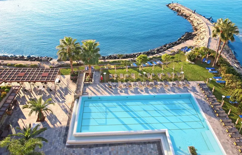 Vue aérienne d'une piscine et d'une terrasse ensoleillée près de la mer.