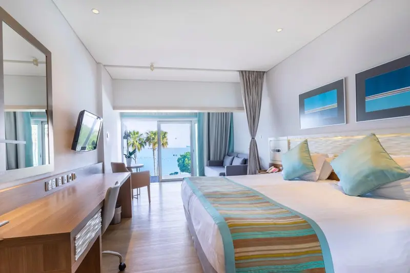 Une chambre lumineuse avec un grand lit et un espace salon donnant sur une vue mer.