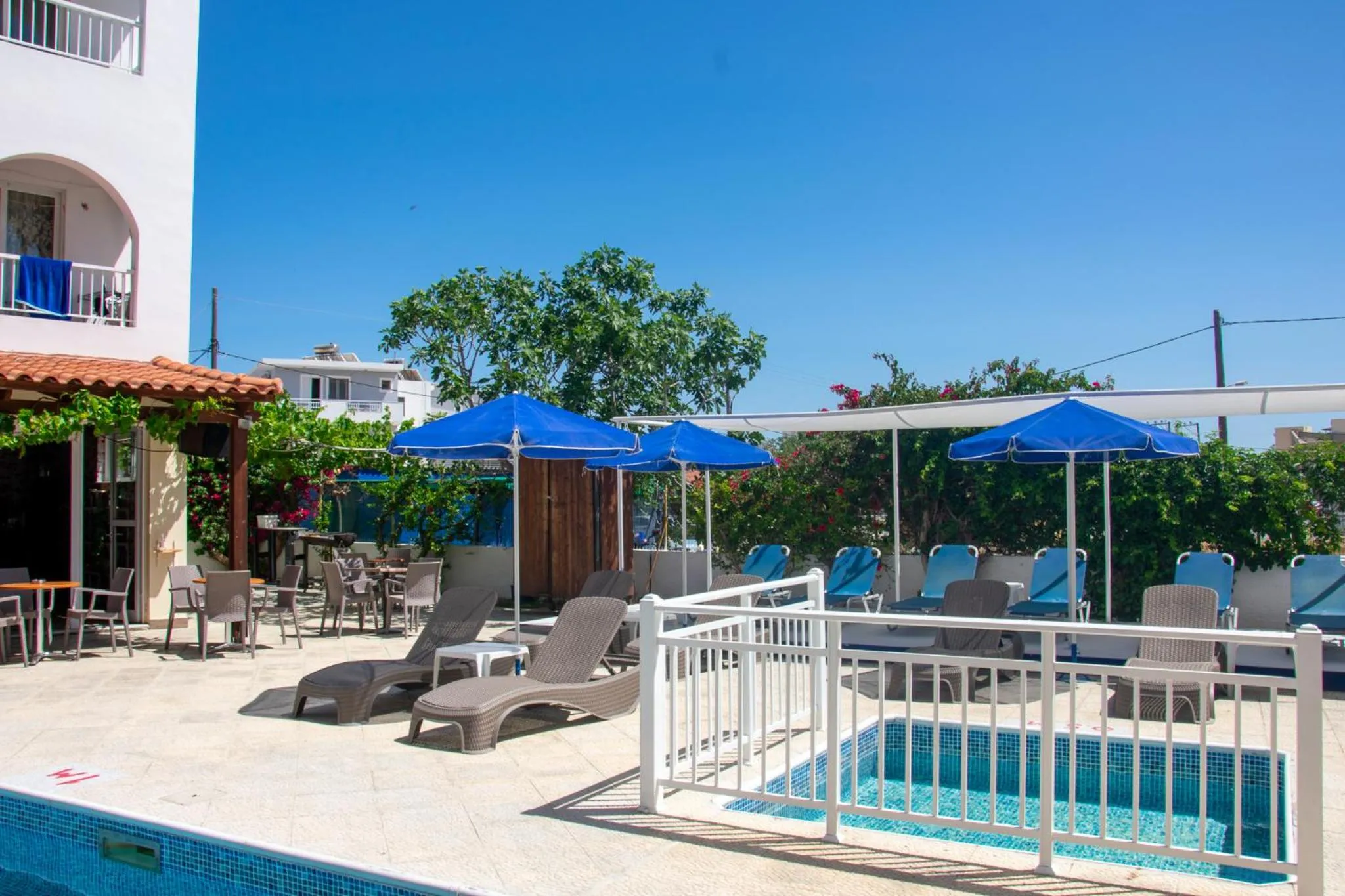 Terrasse avec transats et parasols bleus près d'une piscine.