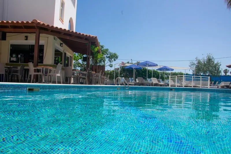 Une piscine turquoise bordée de chaises longues et d'un bar ombragé.