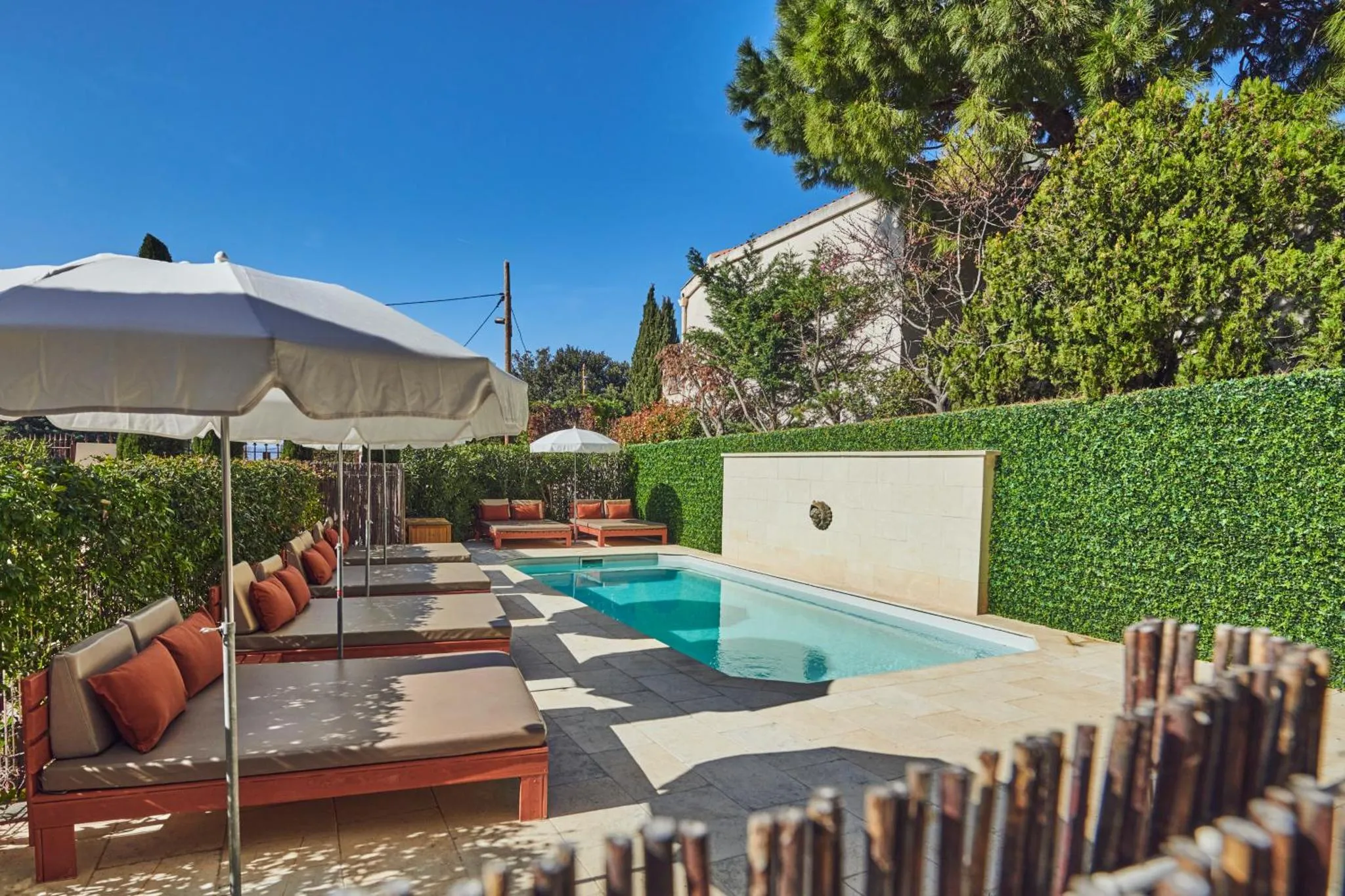 Transats et parasols bordent une piscine rectangulaire dans un jardin soigné.