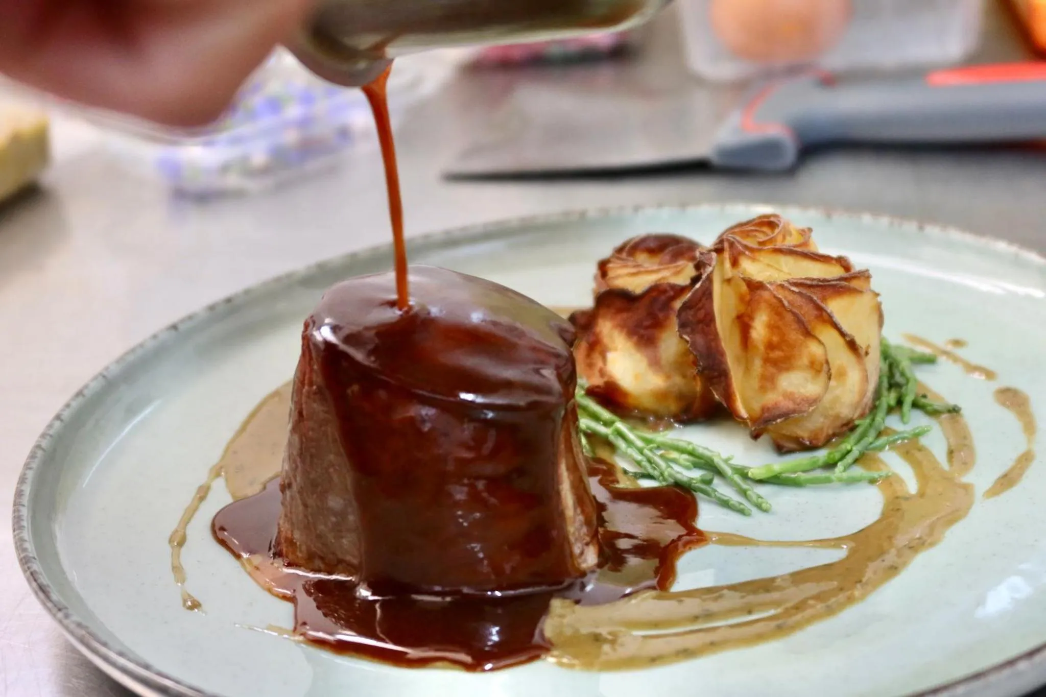 Assiette de viande nappée d'une sauce brune, accompagnée de légumes verts et d'une garniture.