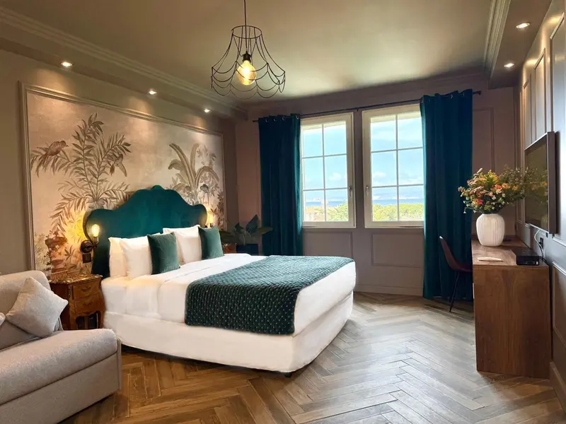 Une chambre à coucher lumineuse avec un grand lit recouvert d'une couette blanche et turquoise, face à une vue sur la mer.