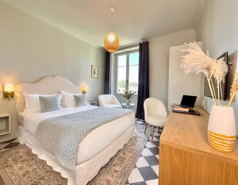 Une chambre lumineuse avec un grand lit et un bureau près de la fenêtre.