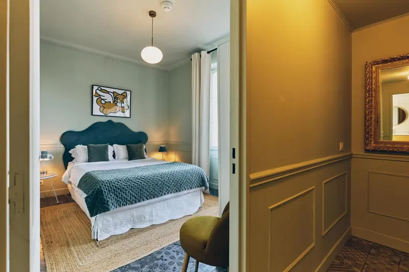 Une chambre à coucher lumineuse avec un lit recouvert d'une couverture verte et un tableau coloré au mur.
