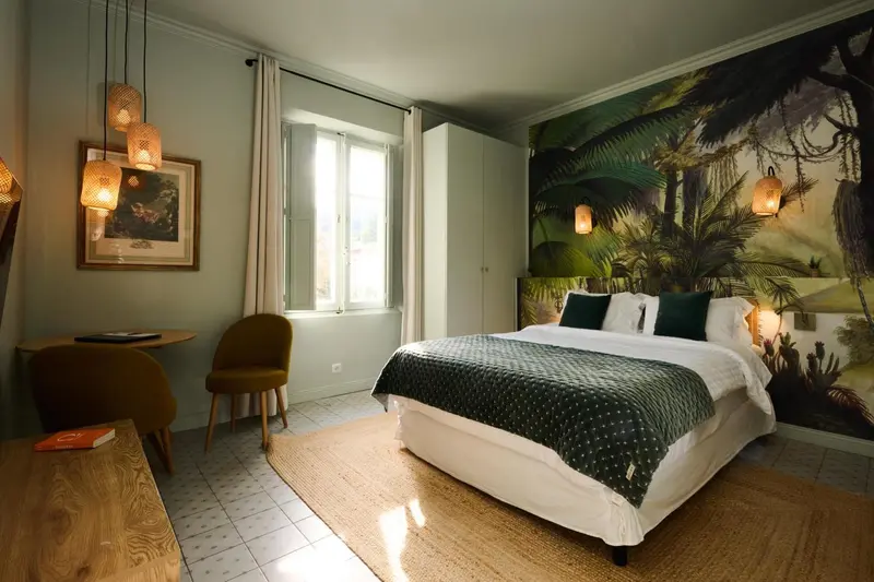Une chambre lumineuse avec un lit recouvert d'une courtepointe et un mur décoré d'une jungle luxuriante.