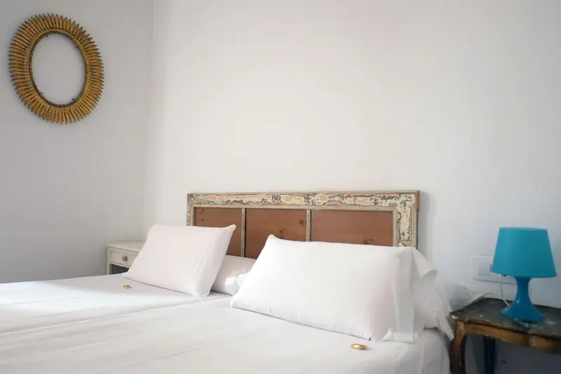 Une chambre lumineuse avec un lit recouvert de draps blancs et une décoration murale.