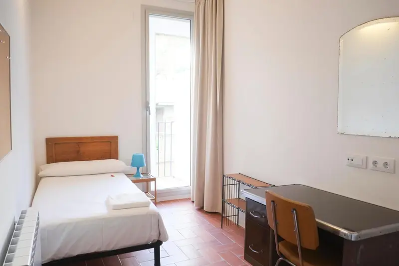 Une chambre simple avec un lit et un bureau près d'une porte-fenêtre.