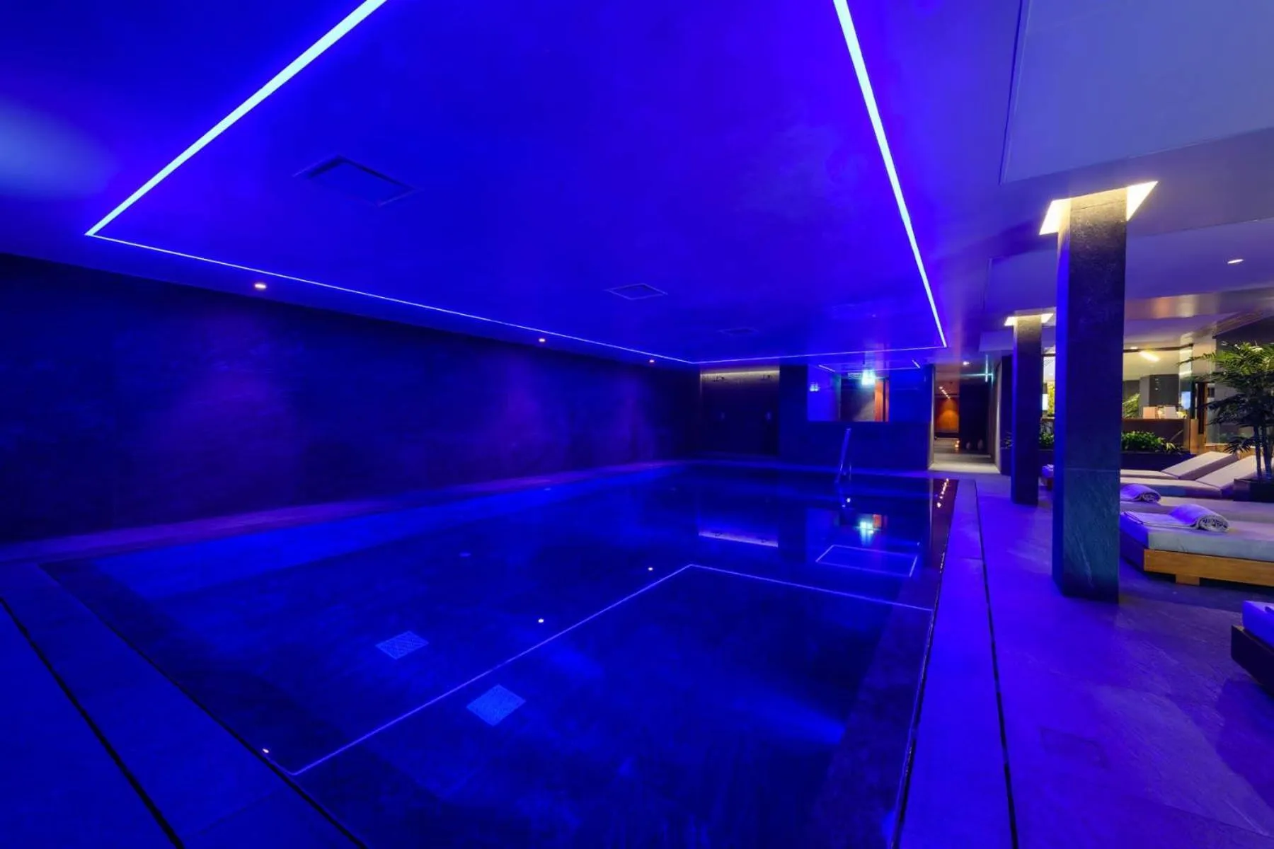 Piscine intérieure illuminée de lumières bleues, avec des transats sur le côté.