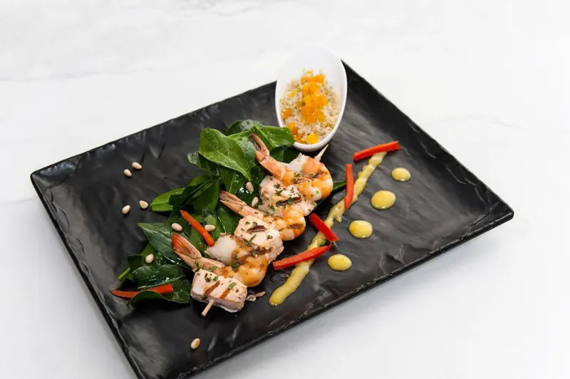 Assiette de crevettes et de poisson grillés sur un lit de verdure.