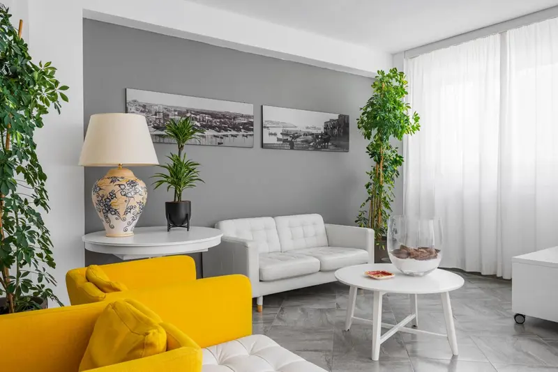 Un salon lumineux avec un canapé blanc et une chaise jaune.