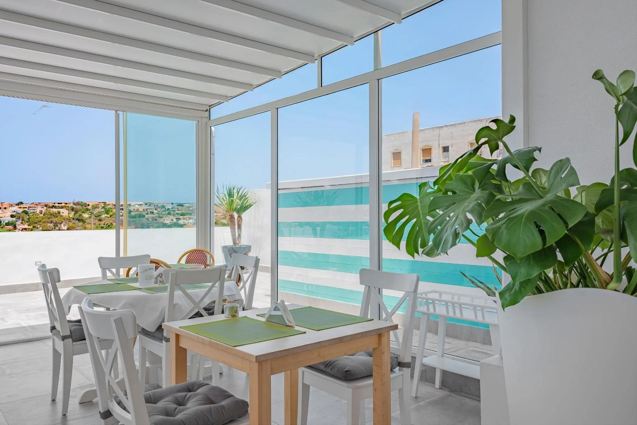 Une salle lumineuse avec des tables dressées face à une piscine et une vue sur la mer.