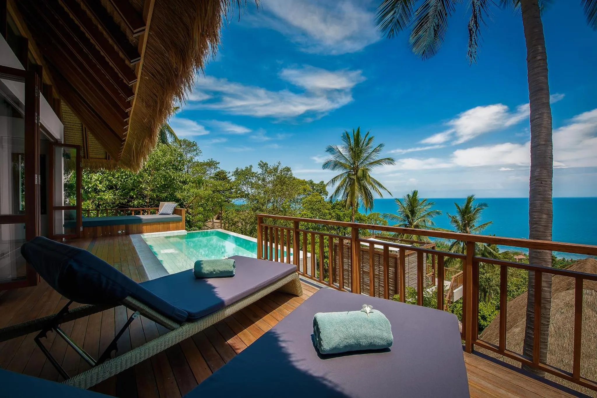 Terrasse en bois avec transats et jacuzzi face à la mer et à la végétation tropicale.