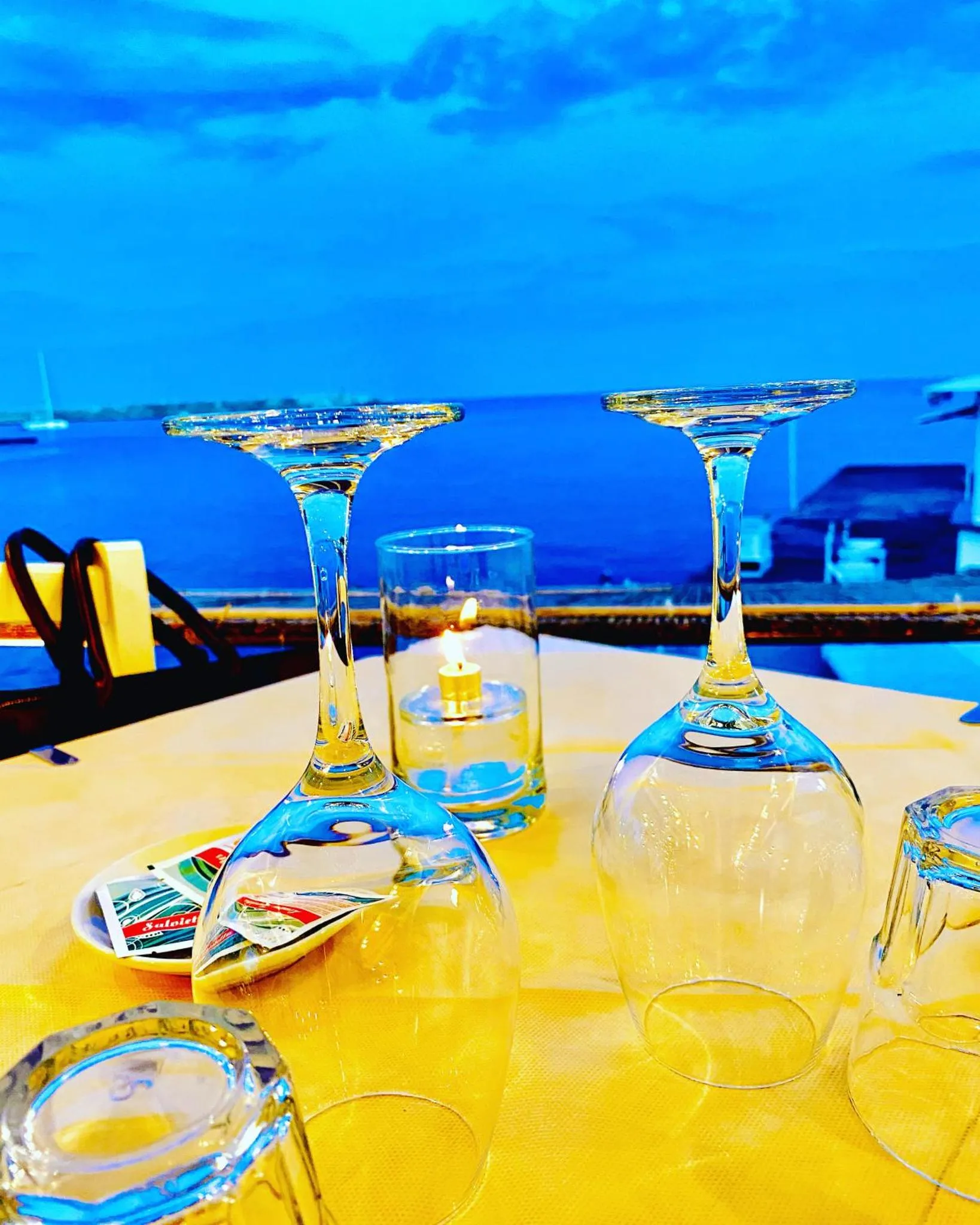 Une table est dressée avec des verres à vin et une bougie allumée, face à la mer.