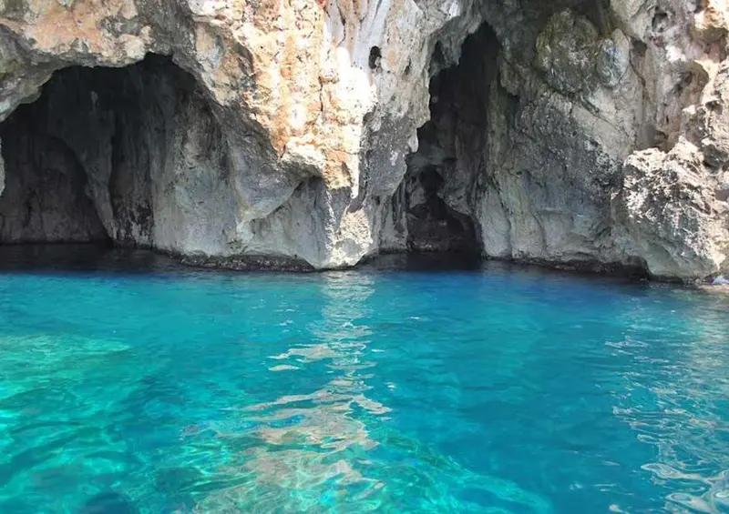 Une eau turquoise limpide baigne l'entrée d'une grotte rocheuse.