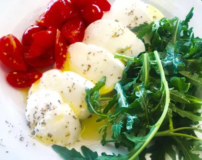 Assiette de salade composée de tomates cerises, de mozzarella et de roquette.
