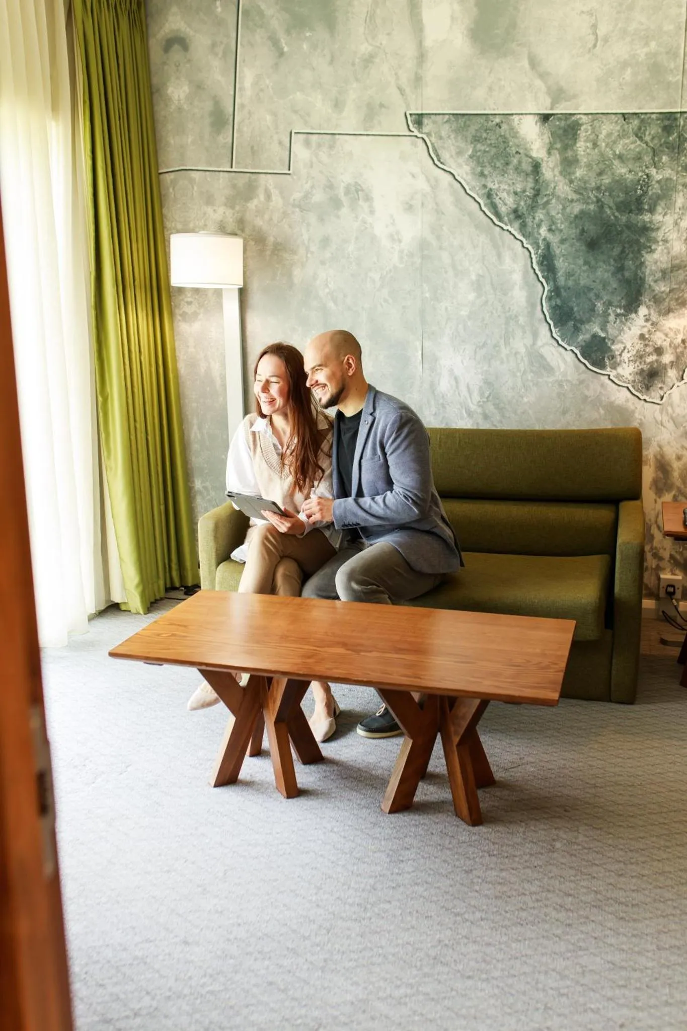 Un couple est assis sur un canapé vert dans un intérieur lumineux.