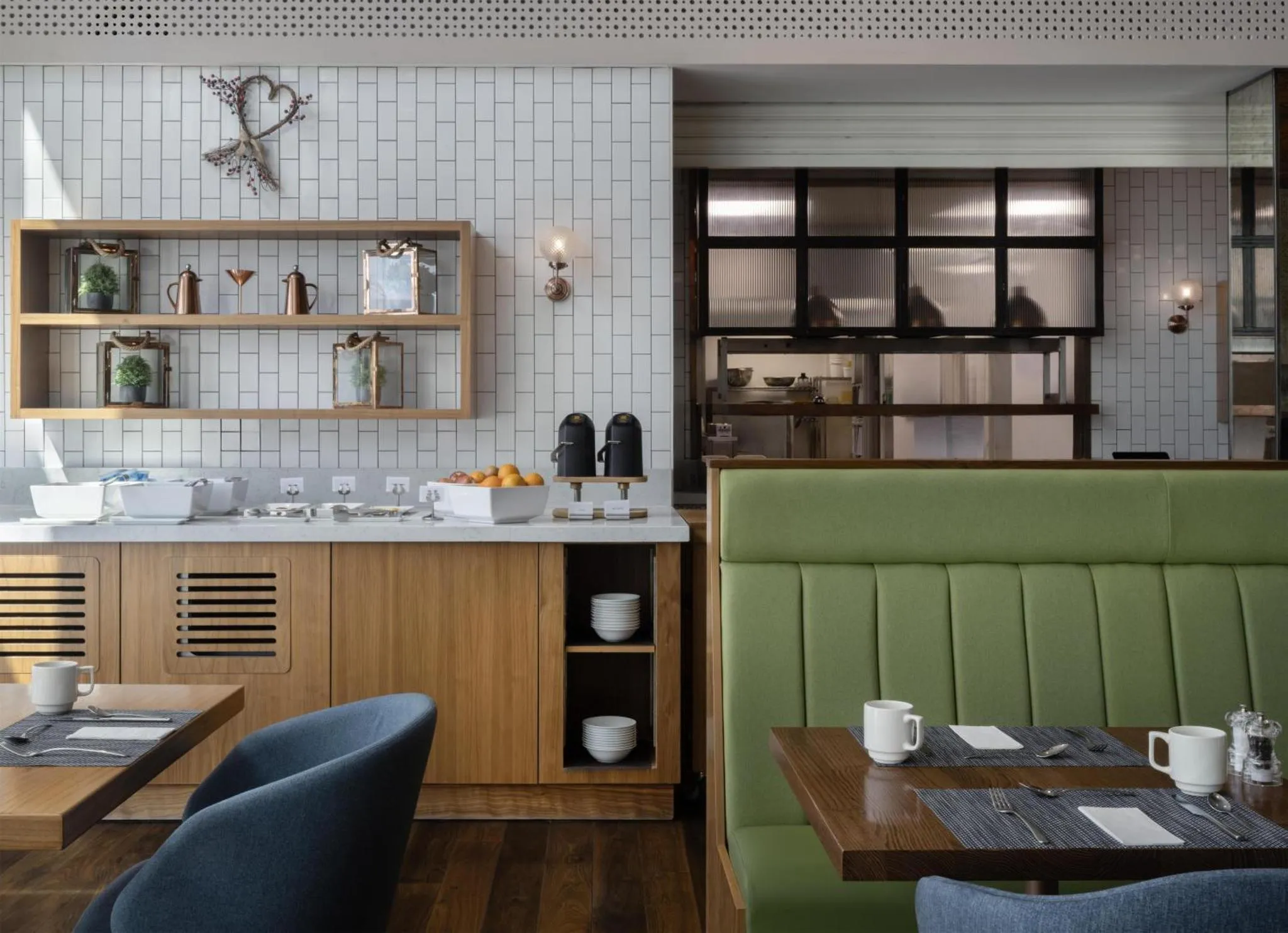 Un buffet de petit-déjeuner est présenté sur un comptoir en bois clair, avec des tables et des chaises pour les convives.
