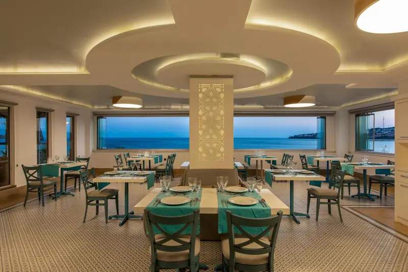 Une salle de restaurant lumineuse avec des tables dressées face à la mer.