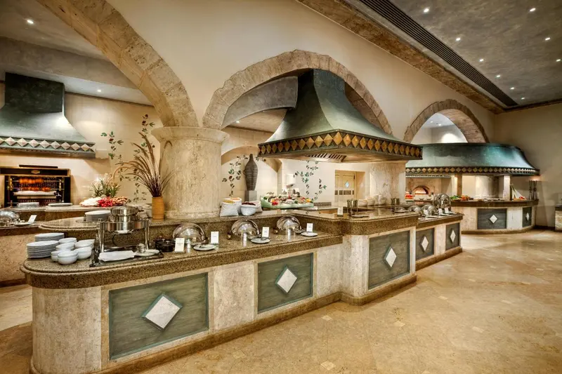 Un long buffet propose une variété de plats dans une salle à l'architecture travaillée.