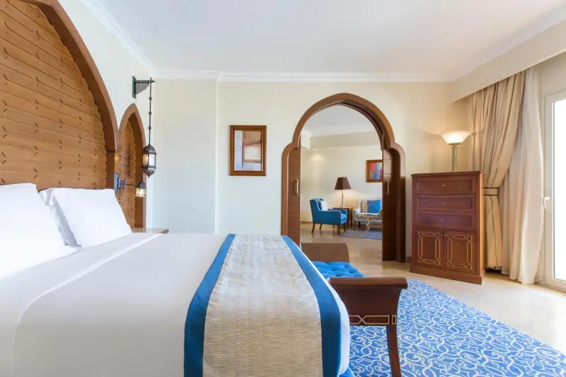 Une chambre lumineuse avec un grand lit et un espace salon attenant.