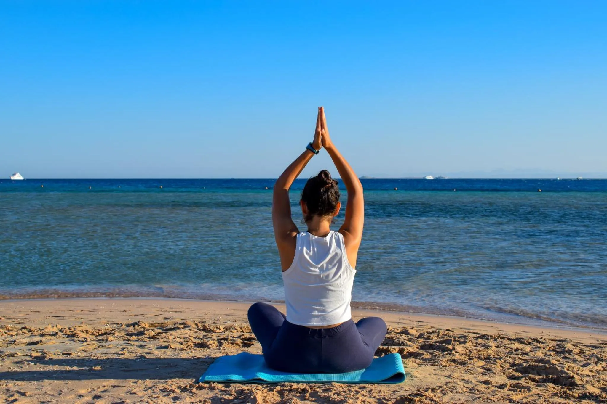 Une personne pratique le yoga sur une plage de sable fin face à la mer.