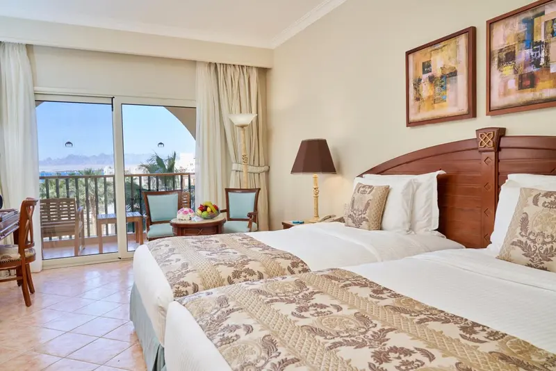 Chambre lumineuse avec un grand lit et une vue sur la mer depuis un balcon.