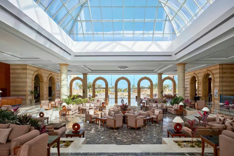 Vaste hall d'accueil avec canapés et plantes sous une verrière.