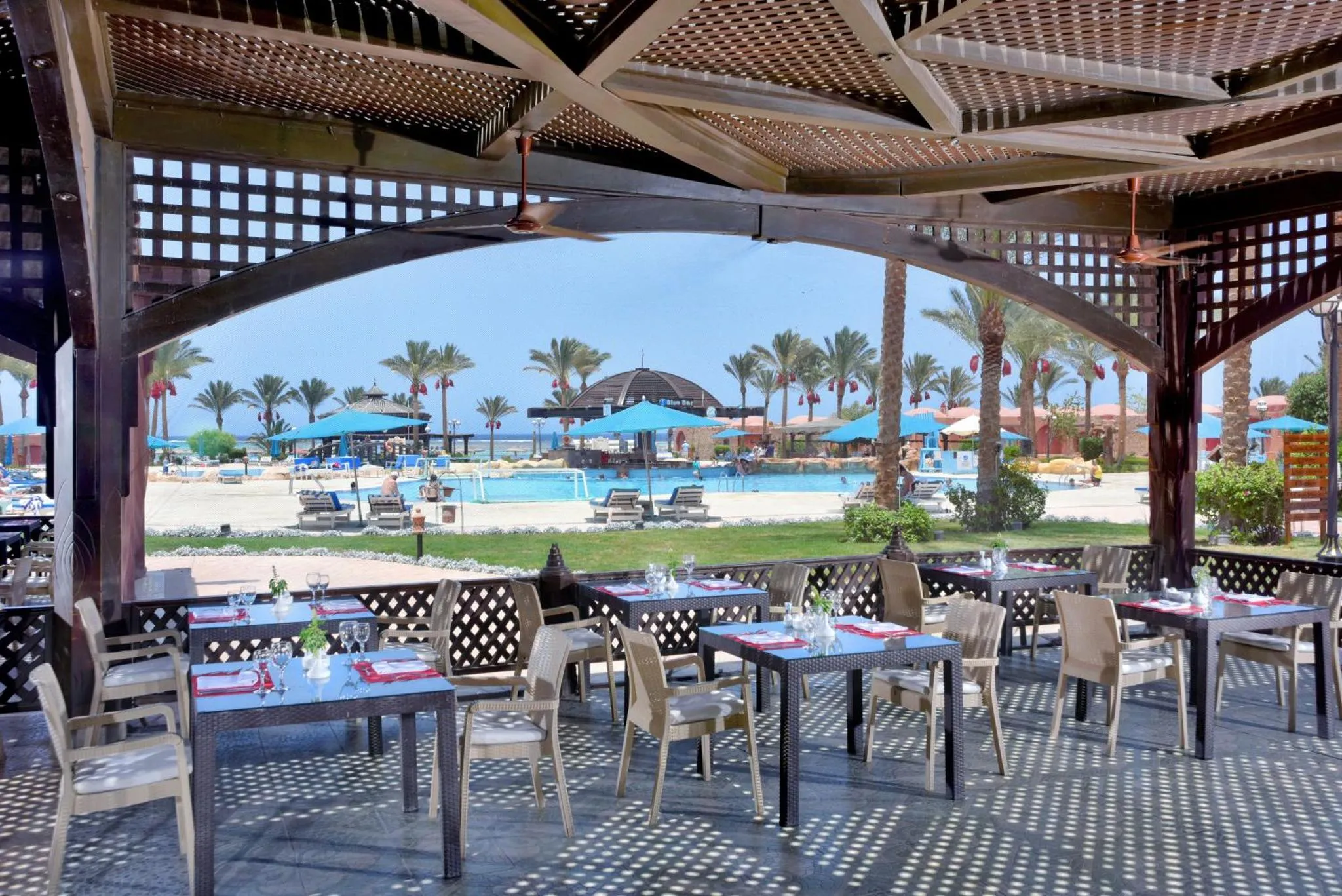 Une terrasse ombragée abrite des tables de restaurant face à une piscine et à la mer.