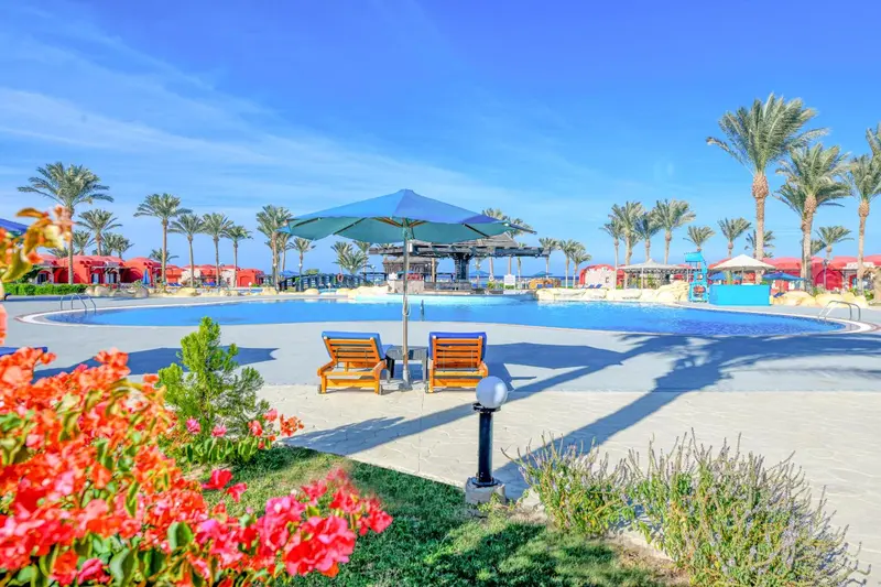 Deux transats se trouvent devant une piscine bordée de végétation luxuriante sous un parasol.