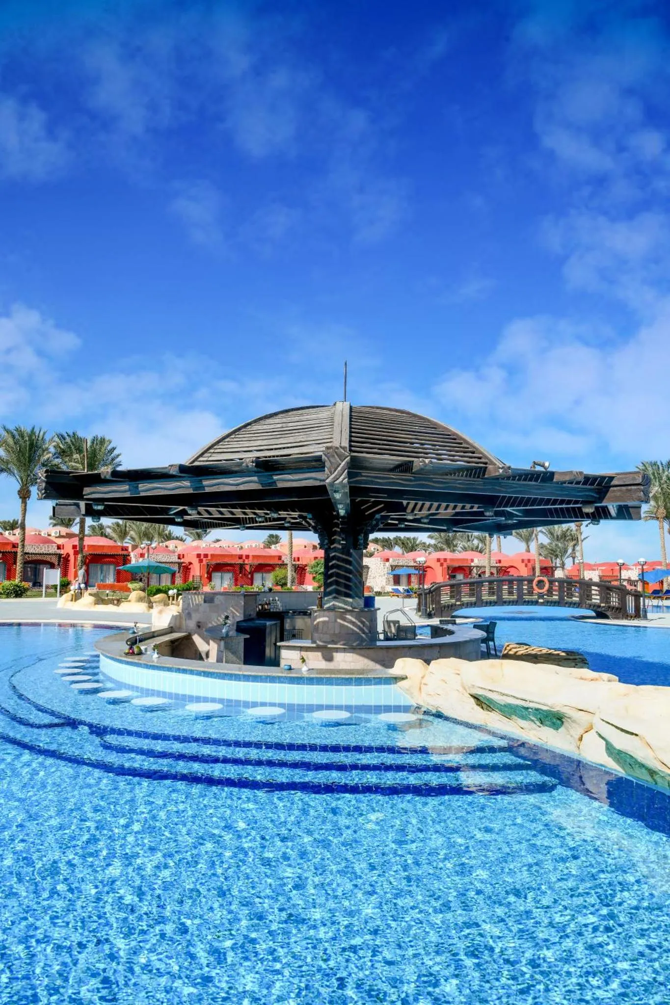Un espace piscine avec un bar ombragé et des transats.